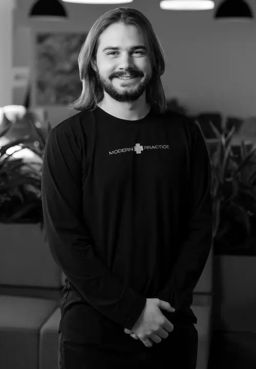 Smiling man with shoulder-length hair and beard wearing a Modern Practice long-sleeve shirt indoors.