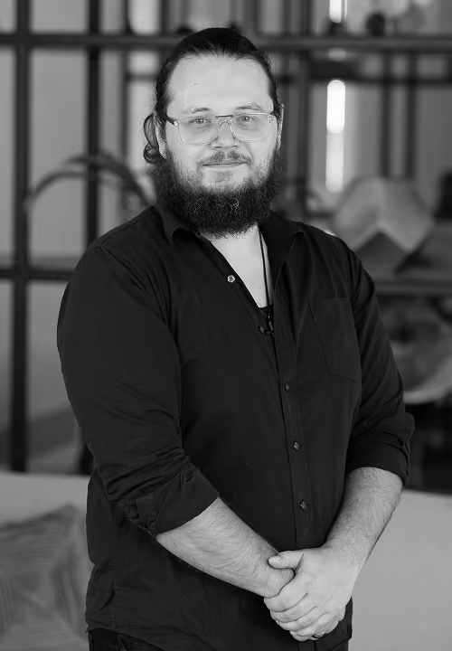 Smiling bearded man with crossed arms wearing a Modern Practice polo shirt in an office setting.