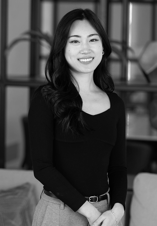 Smiling woman with curly hair wearing a black top and patterned skirt standing indoors.
