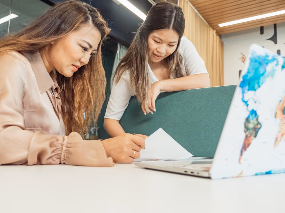 Free Two women reviewing documents together in a modern office setting with a laptop. Stock Photo