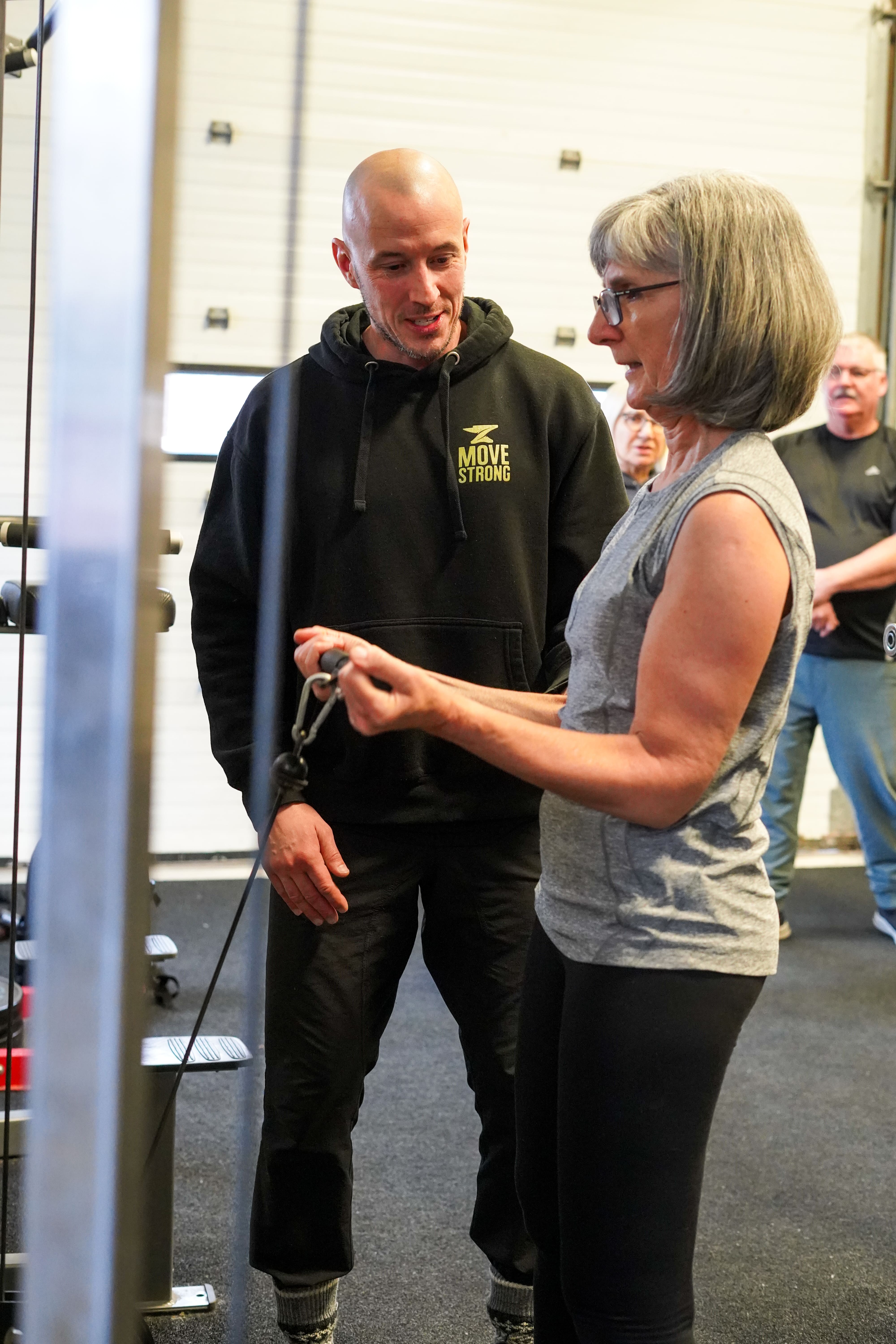 Coach Davor stands with an older woman who is learning how to do a strength exercise. 