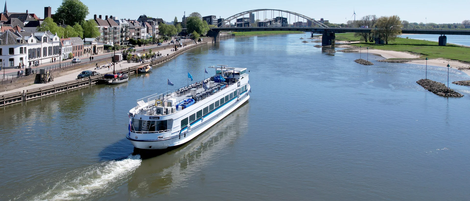 Partyschip de Nirvana, liggend aan de kade in Deventer (gemeente Salland) aan de rivier de IJssel in provincie Overijssel. Met blik op de Lebuïnuskerk en de Wilhelminabrug. Fotograaf: Edwin Mooijaart.