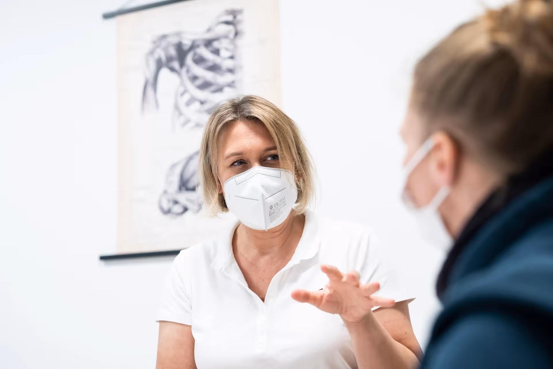 Therapeutin mit Maske im Gespräch mit einer Patientin in der Ergotherapie.