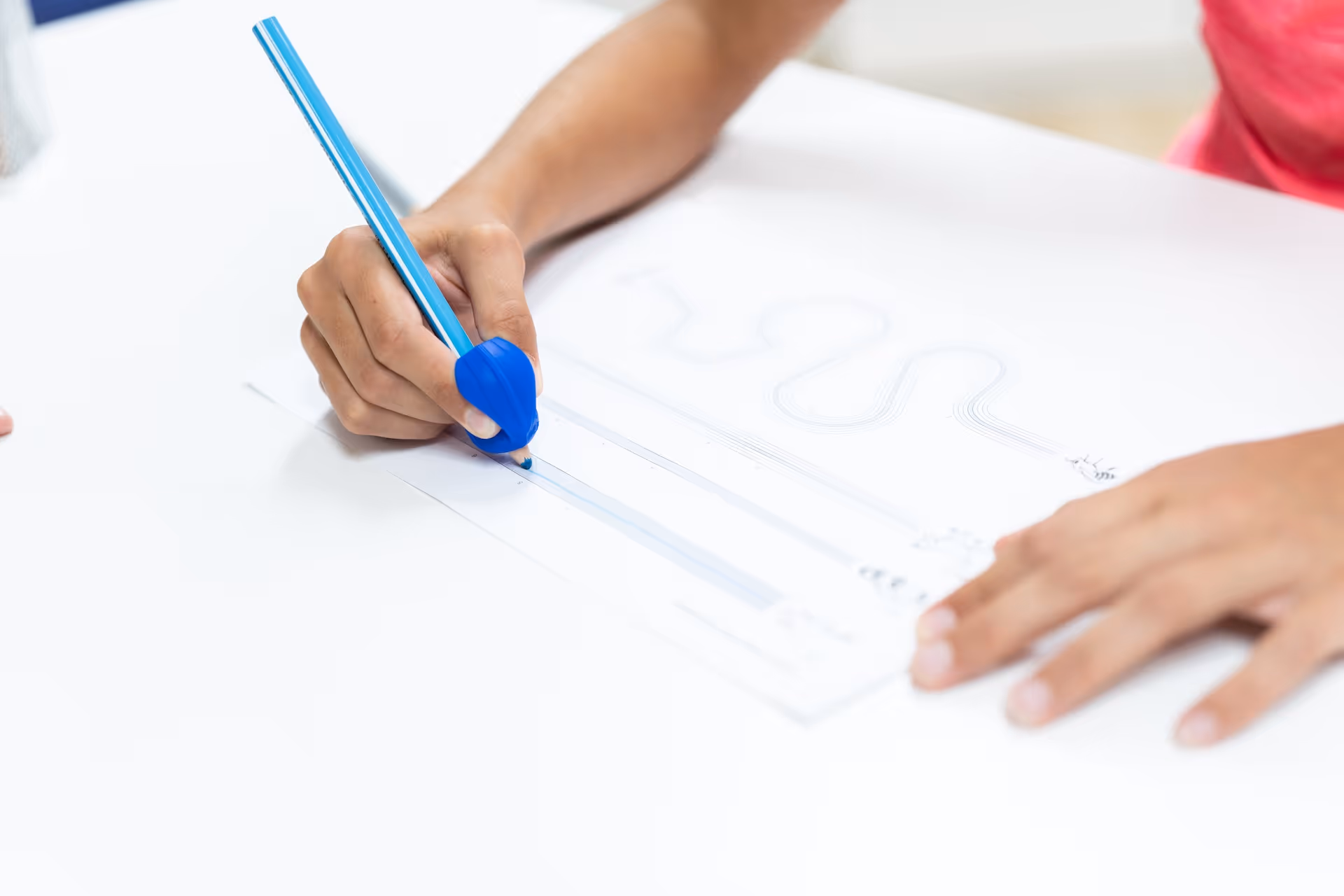 Kind hält einen Stift mit Griffhilfe in der Hand und bearbeitet eine schriftliche Aufgabe.