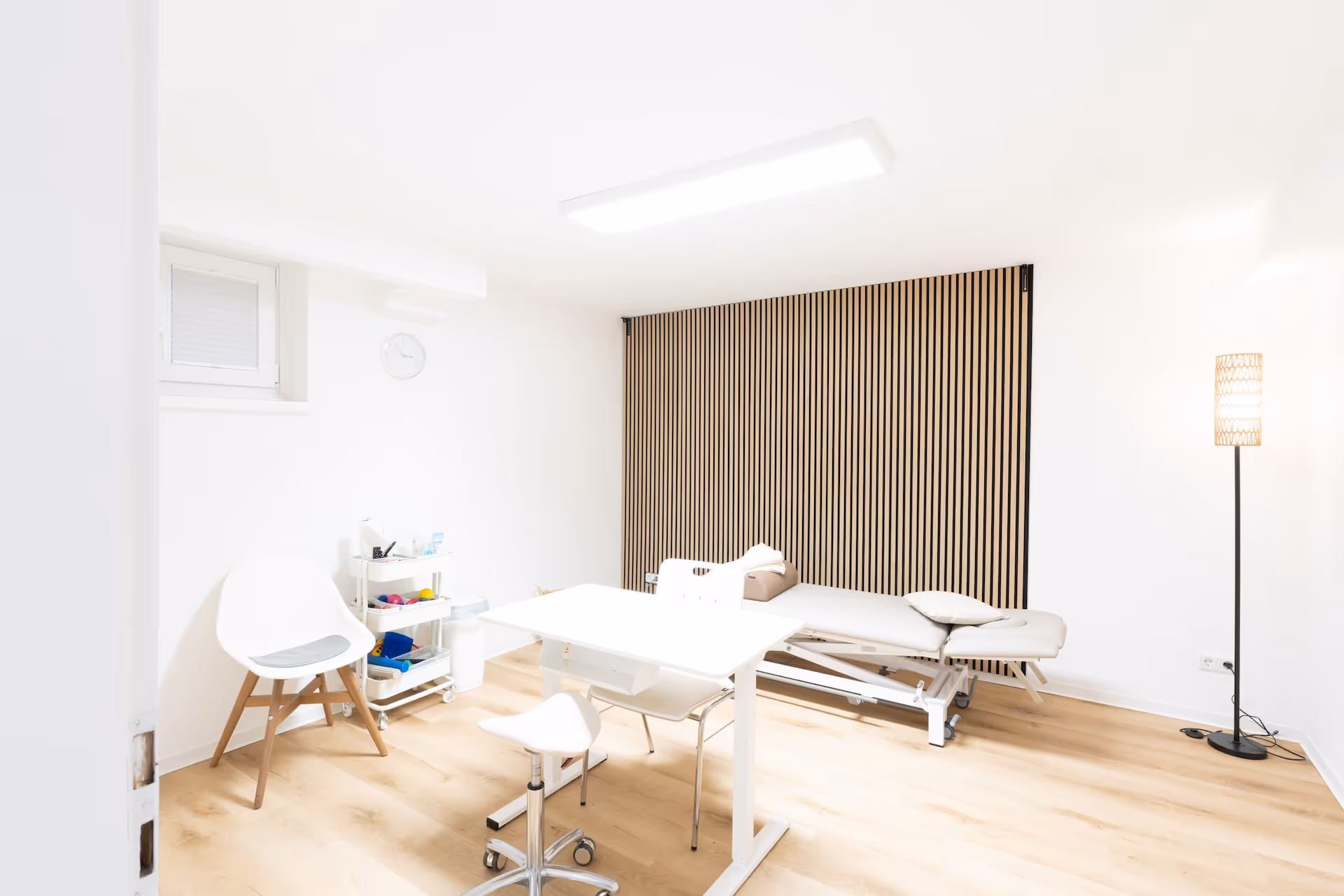 Abbildung eines Therapieraums mit Therapieliege, Behandlungstisch und Akkustikpanelen an einer Wand.