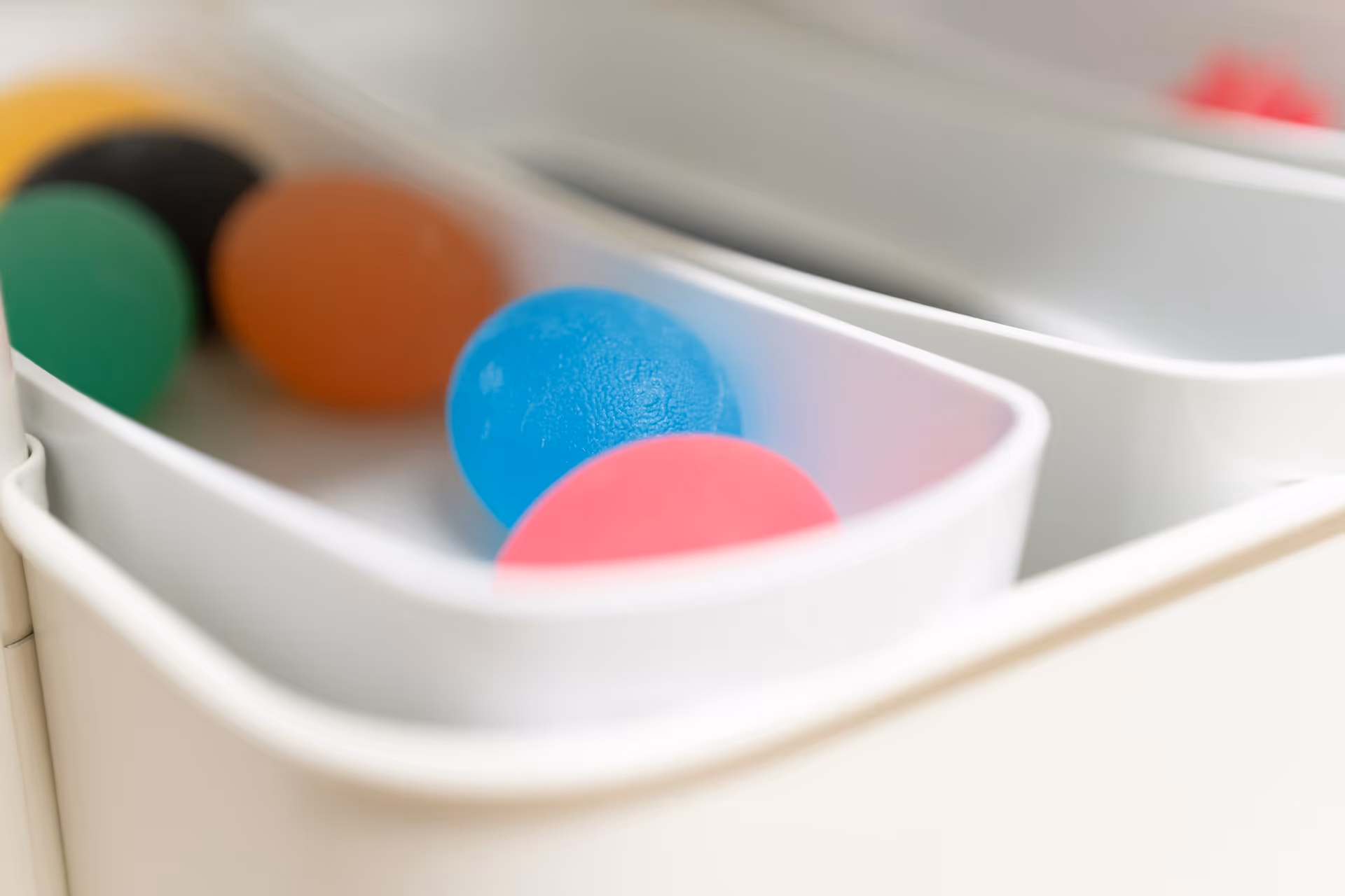 Weißer Behälter mit verschiedenfarbigen Therapie-Bällen.