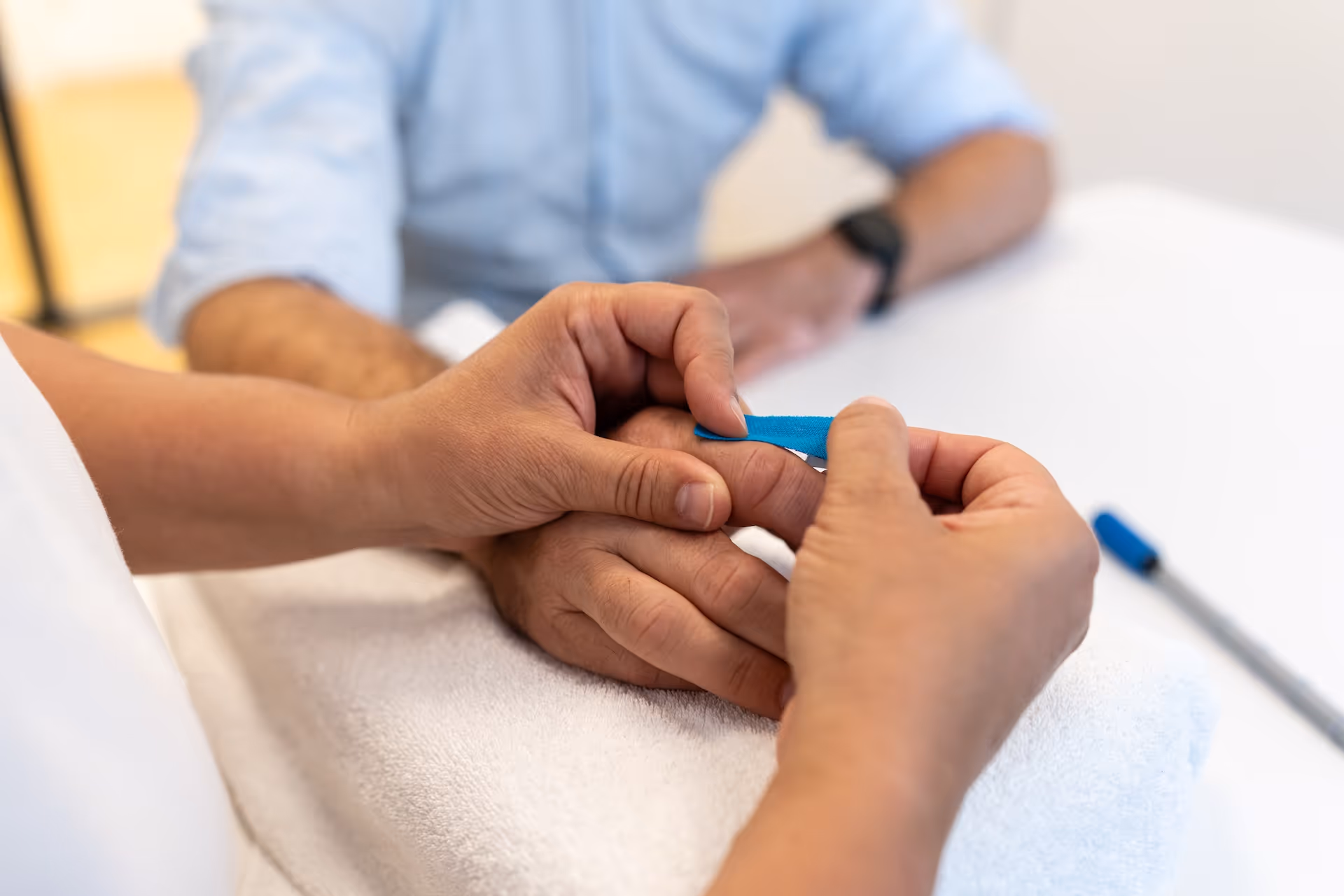 Therapeutin legt einem Patienten ein blaues Kinesio-Tape am Finger an.