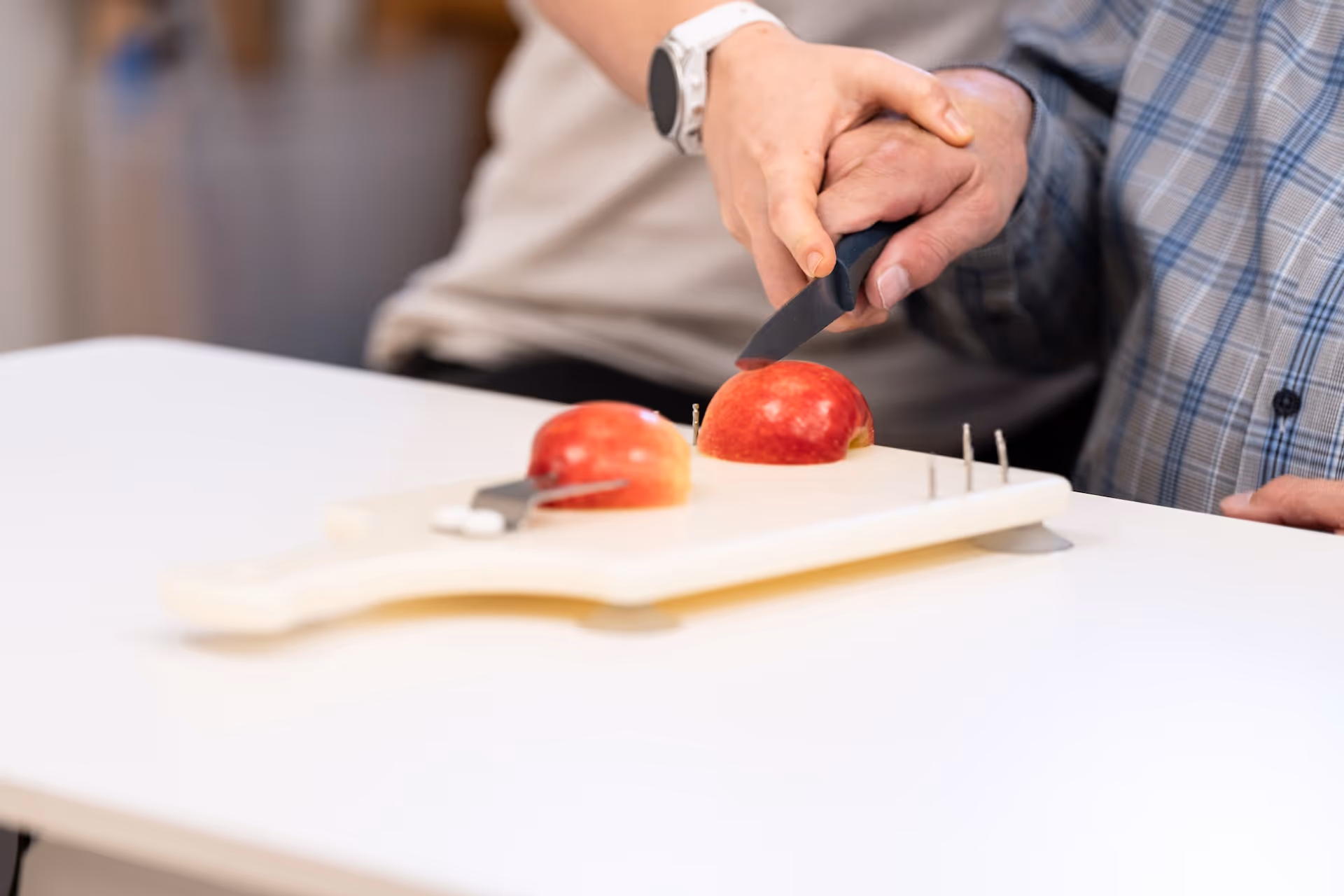 Therapeutin unterstützt einen Patienten beim Schneiden eines Apfels auf einem Einhänder-Schneidebrett.