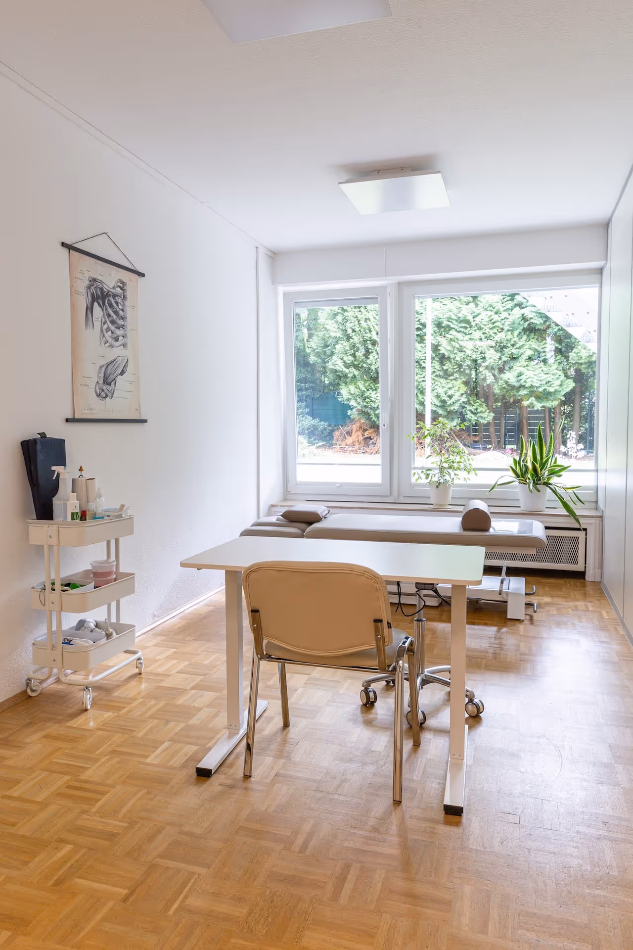 Abbildung eines Behandlungsraums mit großem Fenster und Blick in den Garten, im Vordergrund ein Therapietisch und Stuhl. 