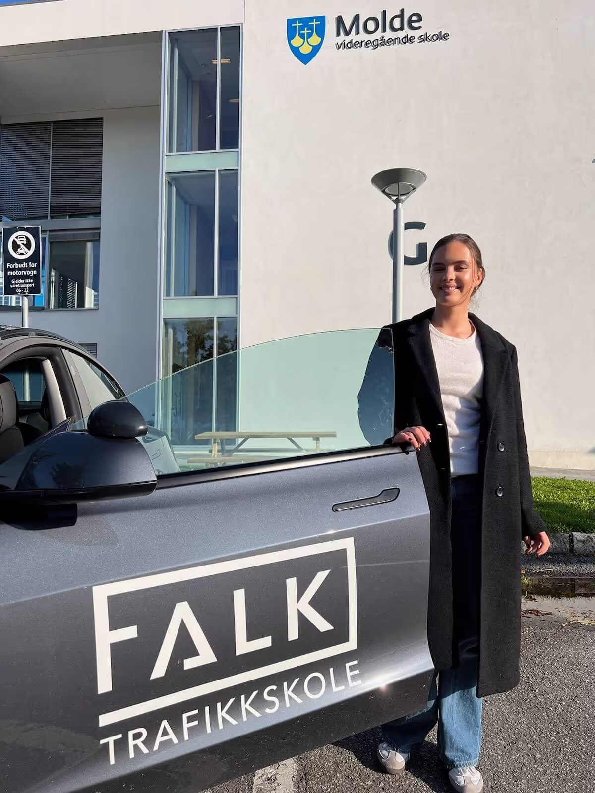 Kvinnelig elev står ved en bil som er står utenfor Molde videregående skole