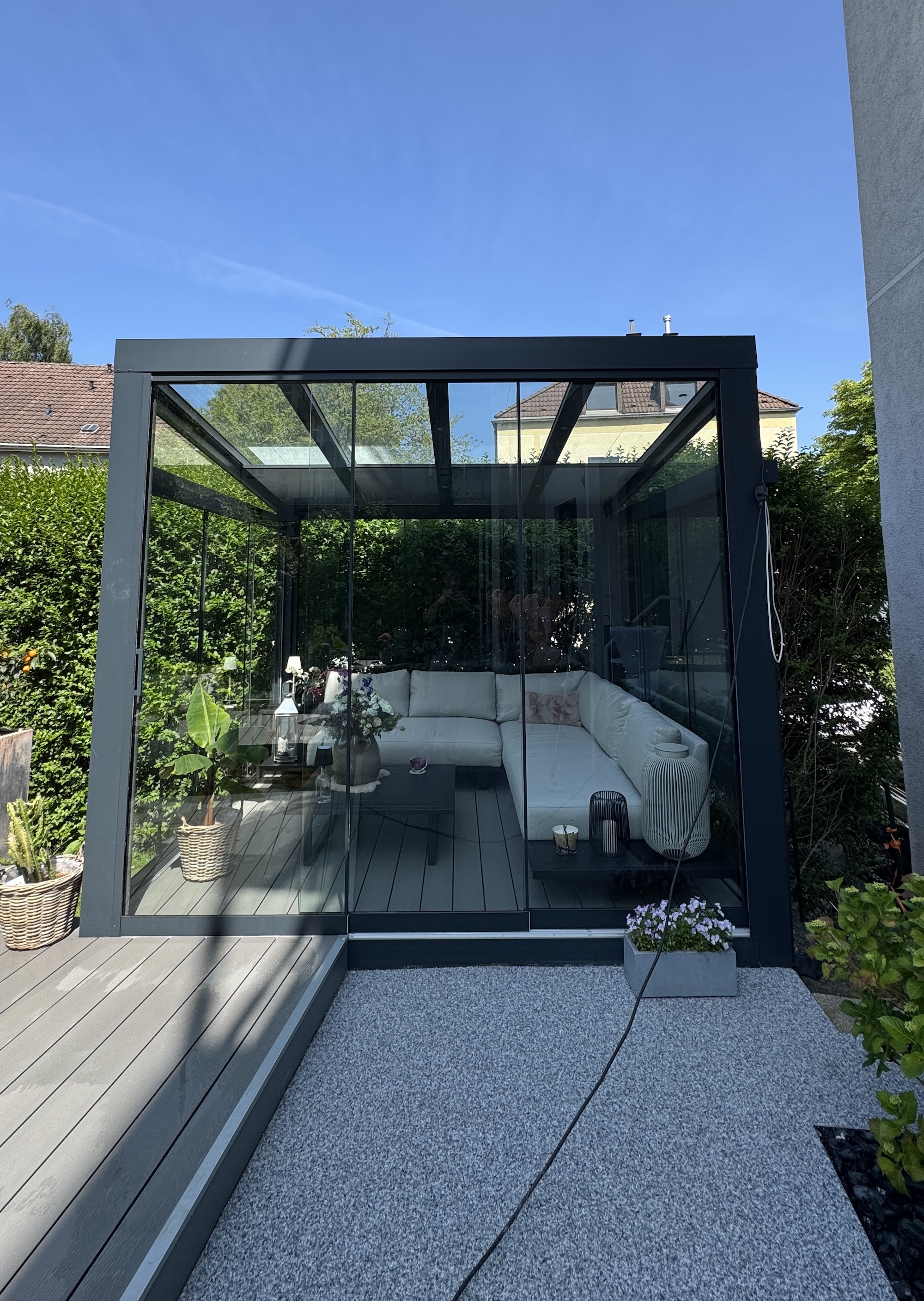 Ein kleiner freistehender Kaltwintergarten mit Glasschiebewänden, Plissee-Beschattung und elektrischer Screen-Markise.