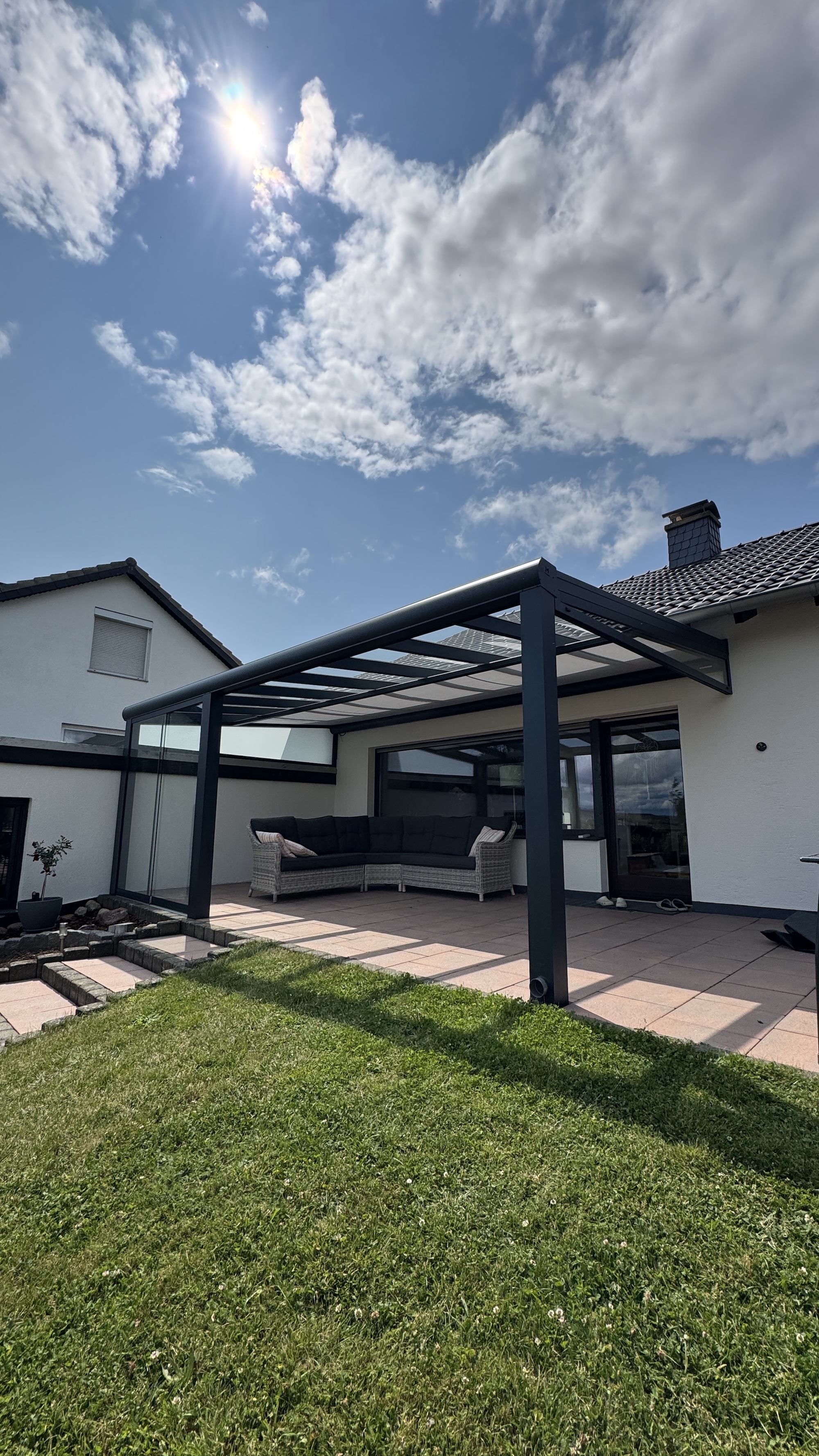 Eine Terrassenüberdachung aus Aluminium mit Glasdach, Unterglasmarkise, Keilelementen aus Glas und Glasschiebewände