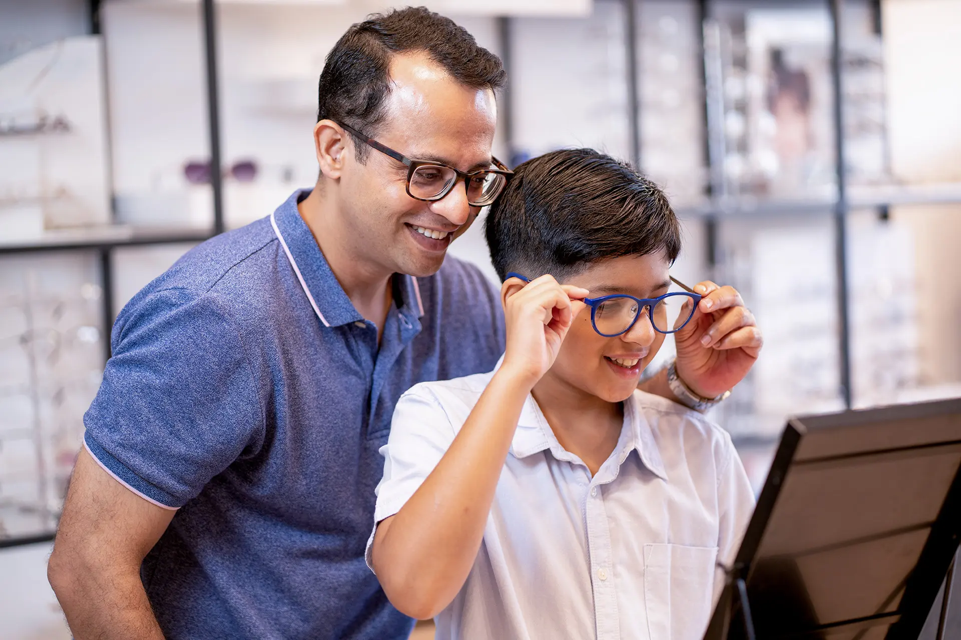 Photo of a smiling male H1B recipient and his son, shopping for eye glasses in a US eye glass store.