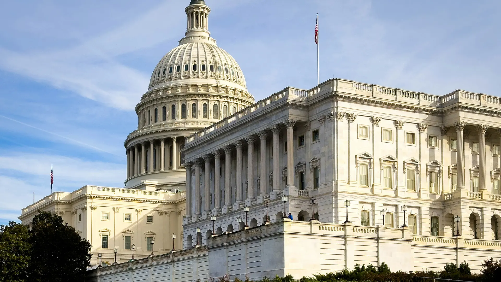 Angled medium shot of the US White House Dome taken from a distance under a blue sky and a few clouds.