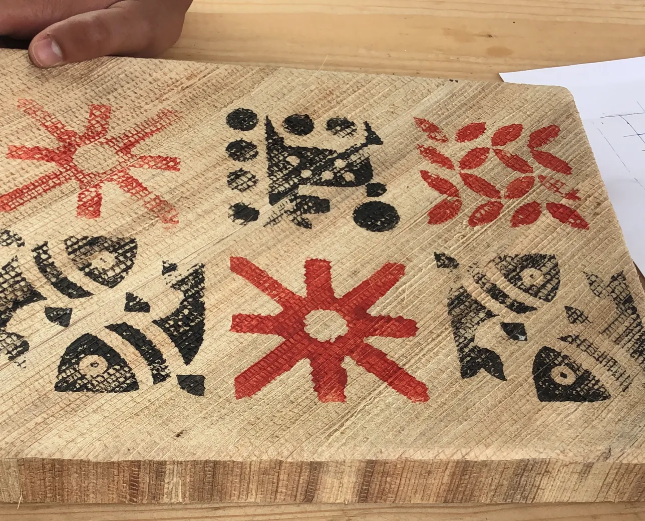 Wooden board with red and black tribal-style geometric and fish patterns painted on it.