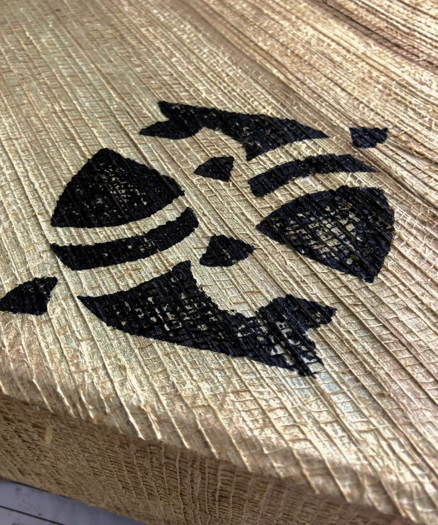 Black geometric and abstract shapes painted on textured light wood surface.