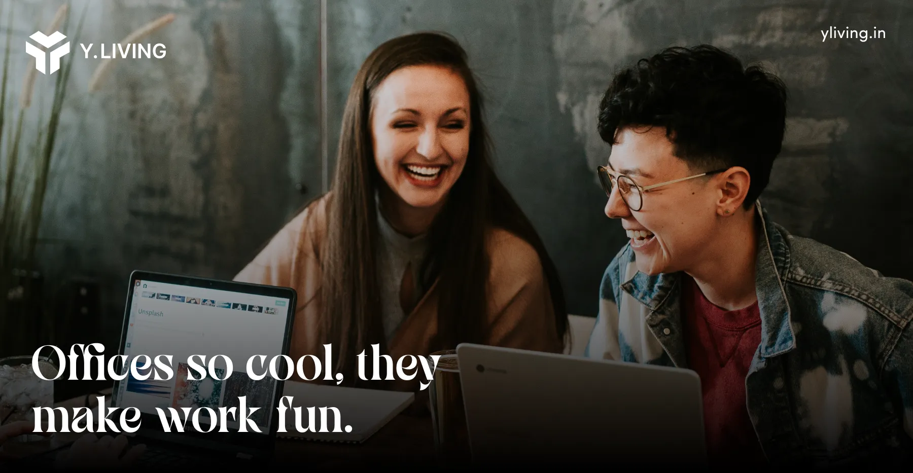 Two people smiling and laughing while working on laptops in a relaxed office setting.