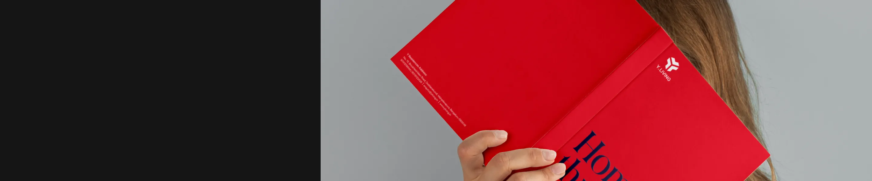 Person holding a red book with a Y-Living logo on the cover, partially obscuring their face.