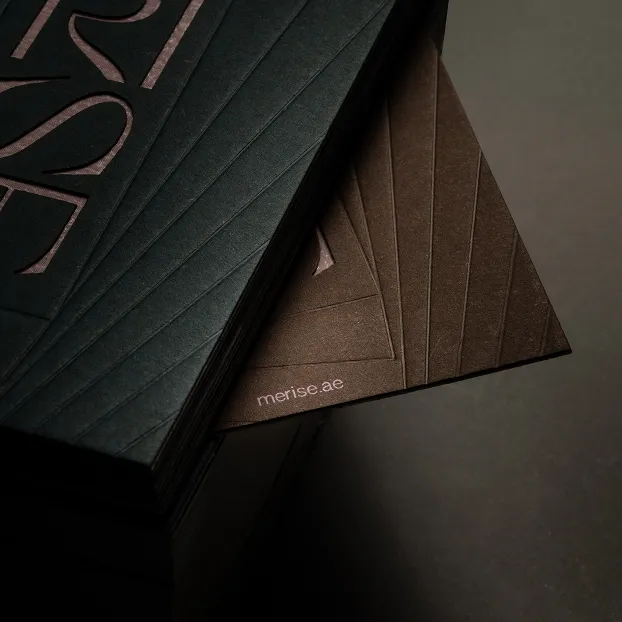 Stack of dark textured cards with embossed diagonal lines and the text 'merise.ae' on one card.