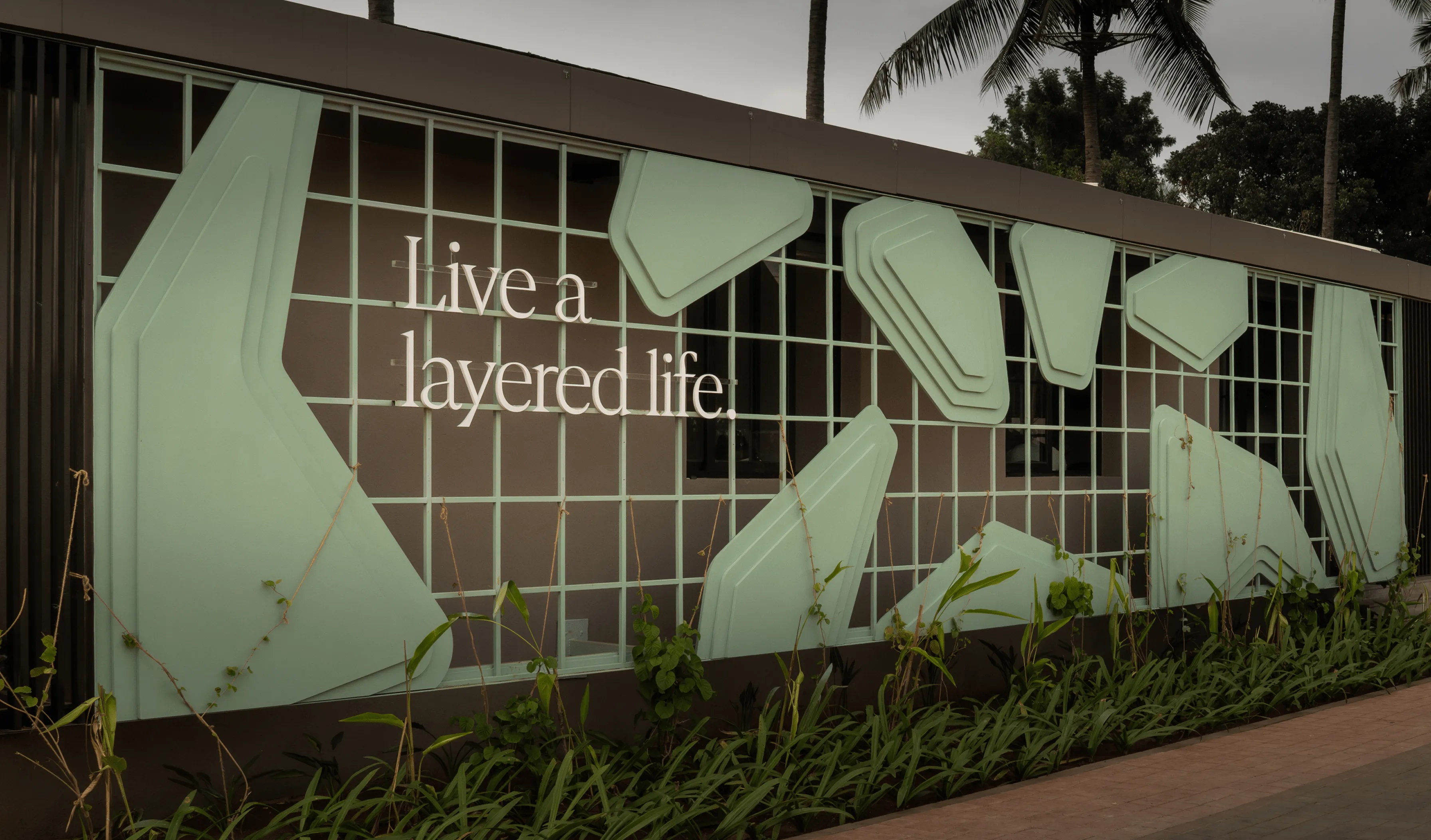 Modern exterior wall with light green layered geometric panels and text saying 'Live a layered life.'