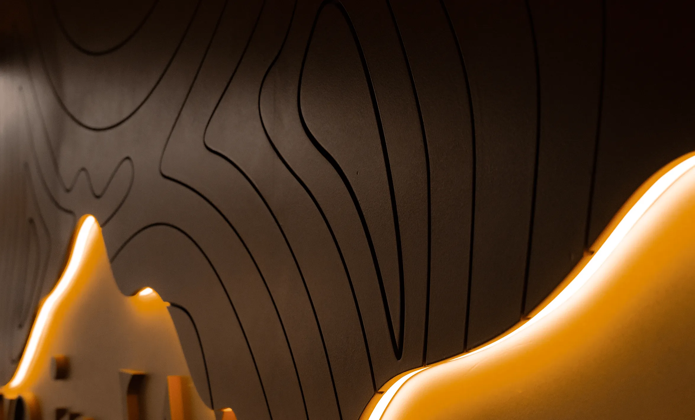 Wall with abstract raised contour lines illuminated by warm yellow LED lighting creating a glowing effect.