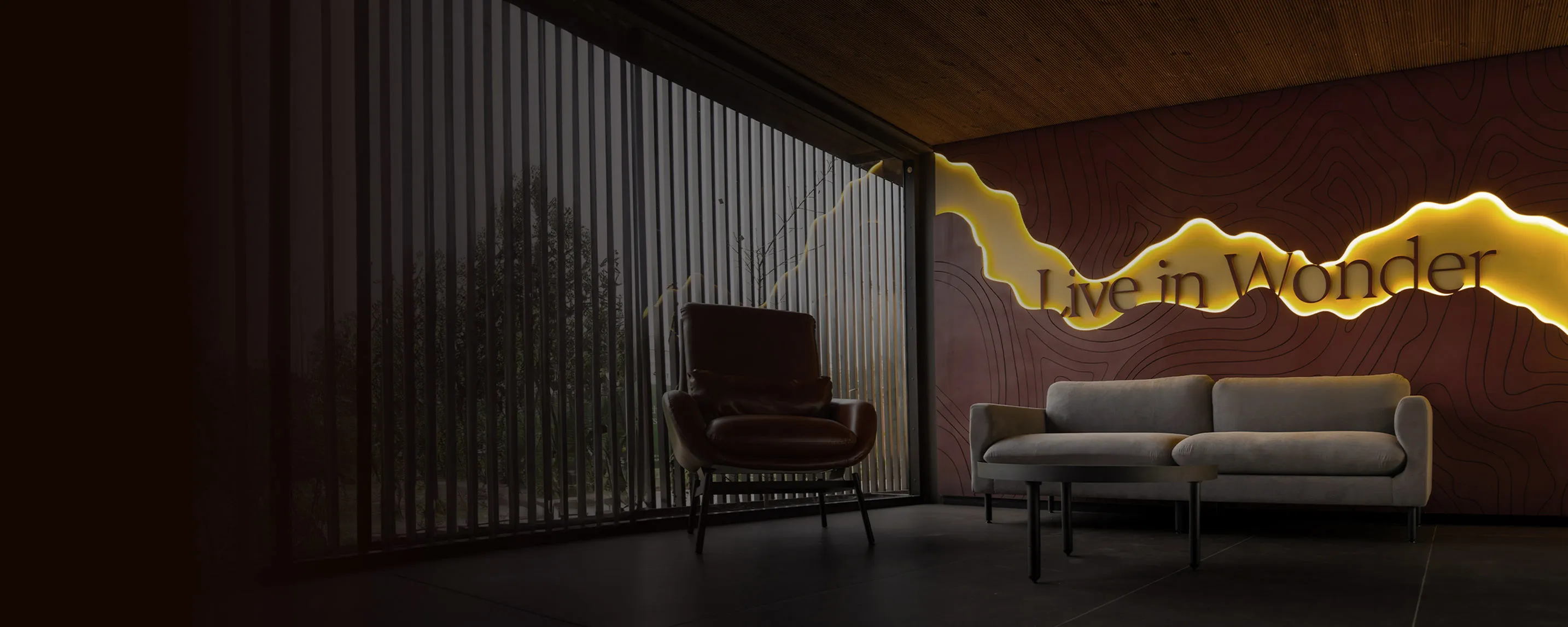 Modern interior with a leather armchair, gray sofa, black coffee table, and illuminated wall art saying 'Live in Wonder'.