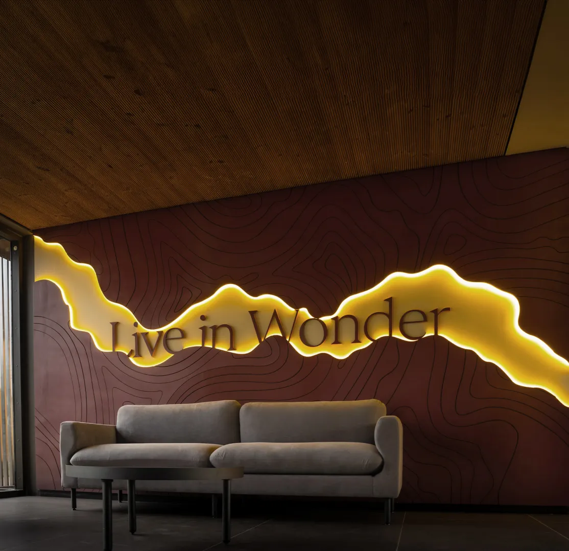 Modern seating area with a gray sofa and coffee table in front of a dark wall featuring illuminated wavy design and the words 'Live in Wonder'.