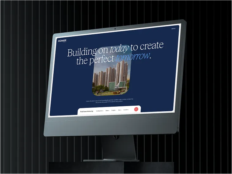 Computer monitor displaying a real estate website with the text 'Building on today to create the perfect tomorrow' and an image of tall apartment buildings.