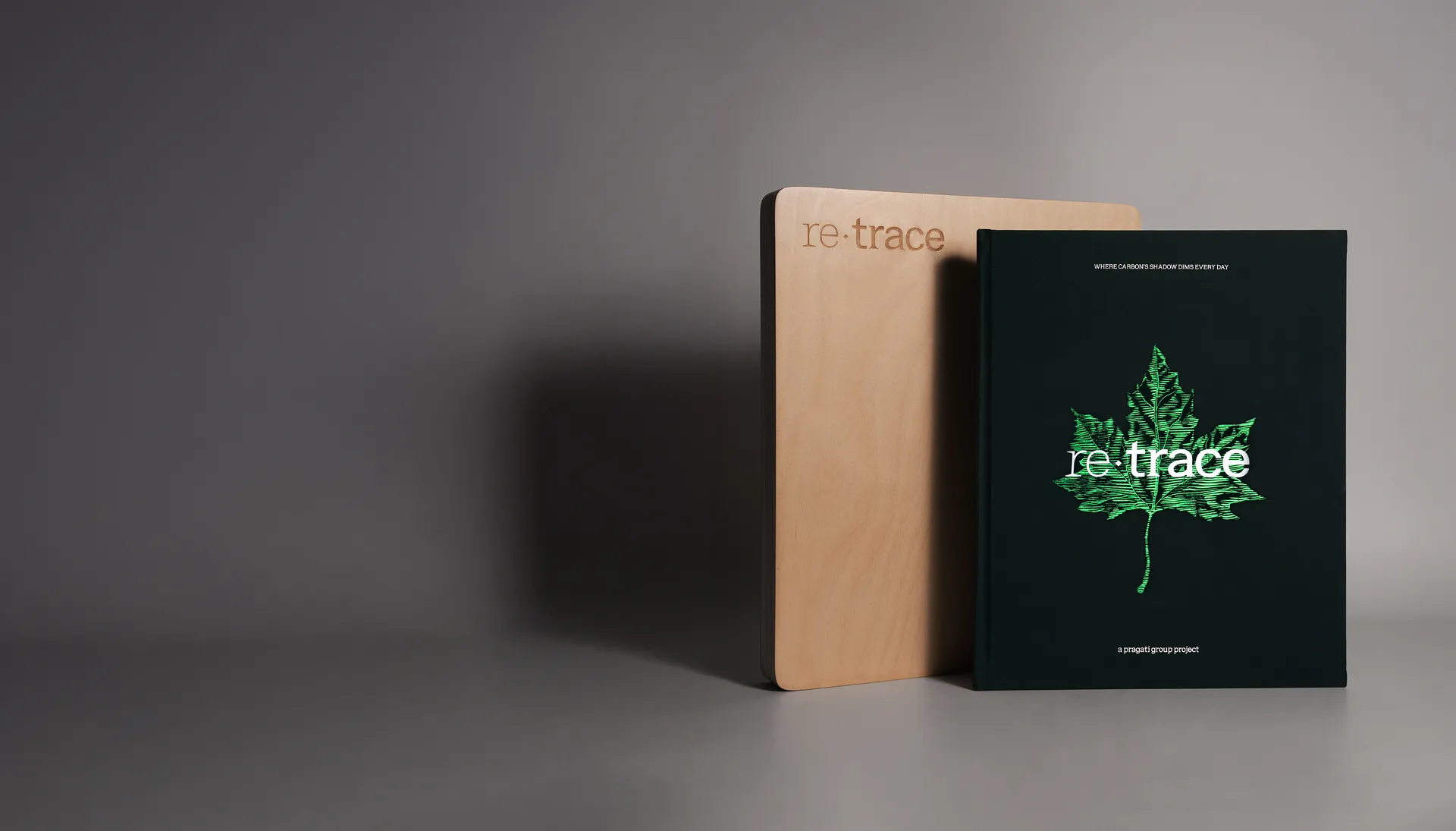 Book titled 're:trace' with a green leaf illustration next to a wooden case engraved with 're:trace' on a grey background.