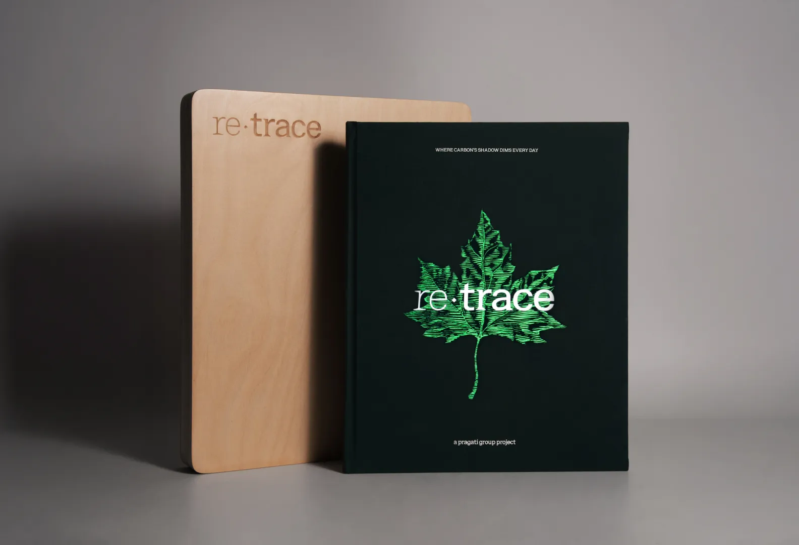 Black book with a green leaf illustration and the title 're·trace' leaning against a wooden block with an engraved 're·trace' text.