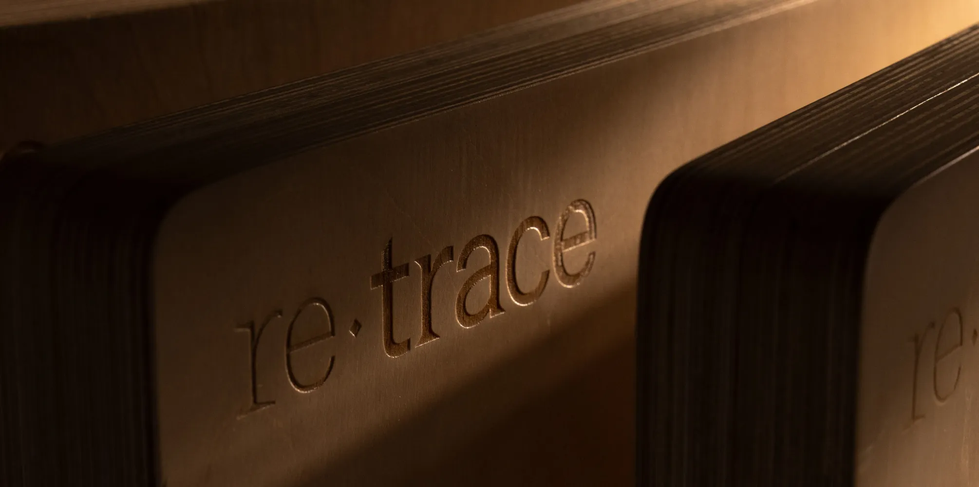 Close-up of two thick, wooden blocks with the word 're:trace' engraved on their surfaces in warm lighting.
