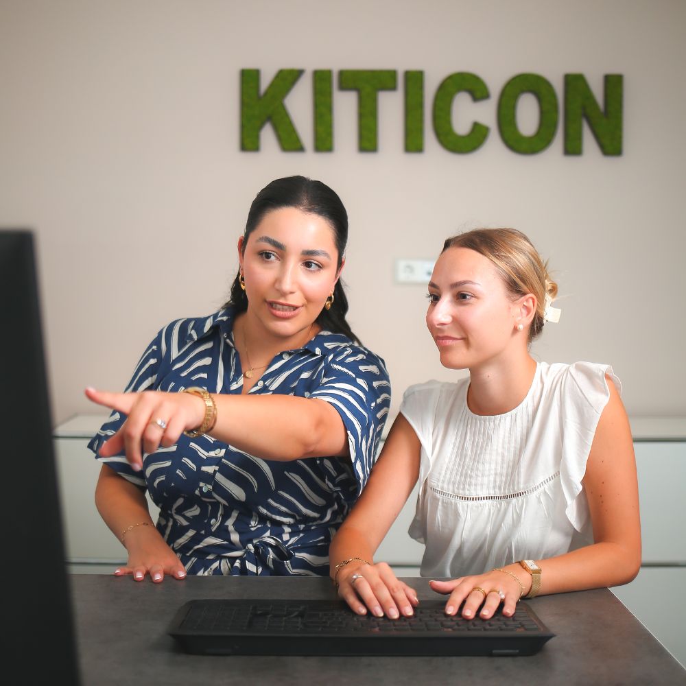 Die Mitarbeiterinnen Julia und Jessy schauen sich gemeinsam etwas auf dem Monitor an