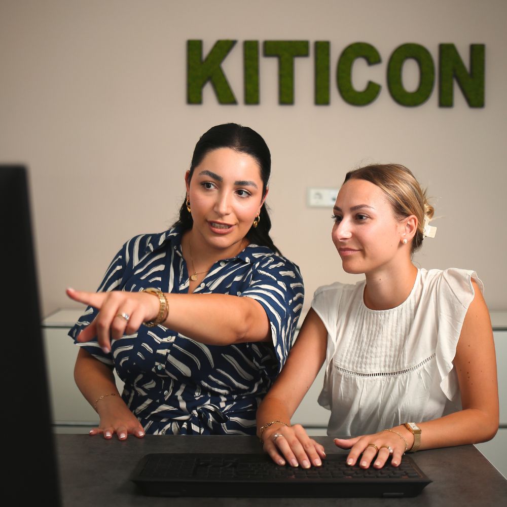 Die Mitarbeiterinnen Julia und Jessy schauen sich gemeinsam etwas auf dem Monitor an