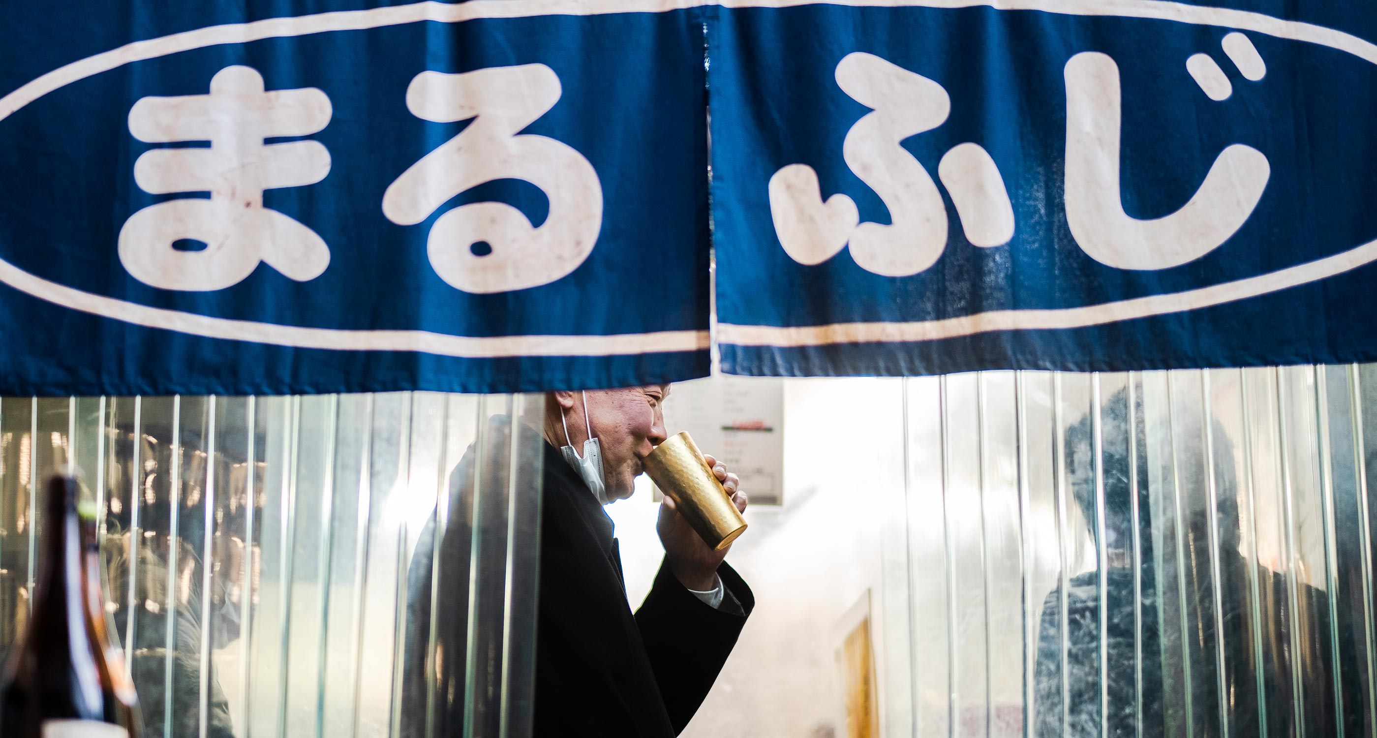 A man drinking from a gold cup in a Japanese izakaya called "Marufuji".