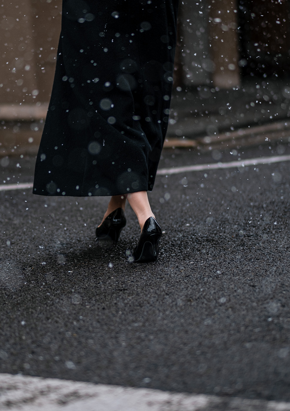 Photo of a woman holding an umbrella and her skirt with the other hand, walking down the street in the pouring rain,