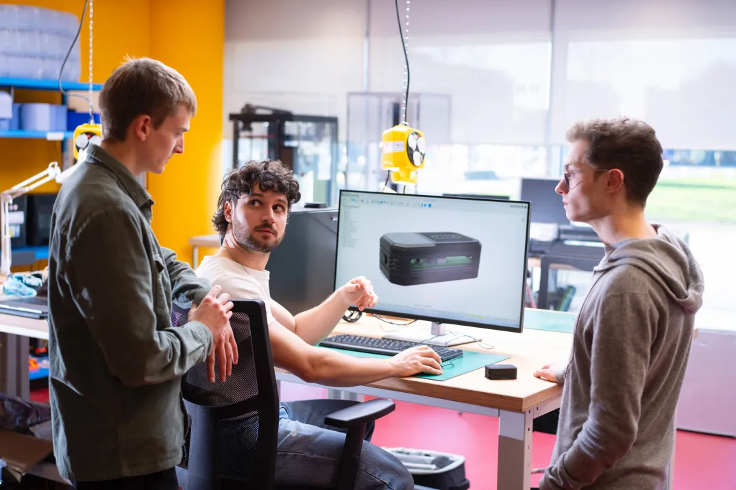 Three men standing around a screen, discussing a CAD model.