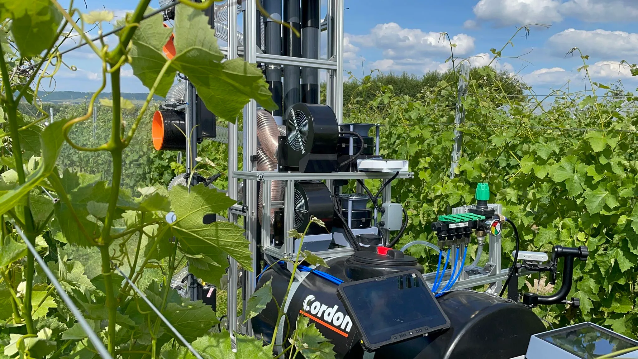 Cordon's vinyard sprayer robot being towed by a tractor in a green vineyard.