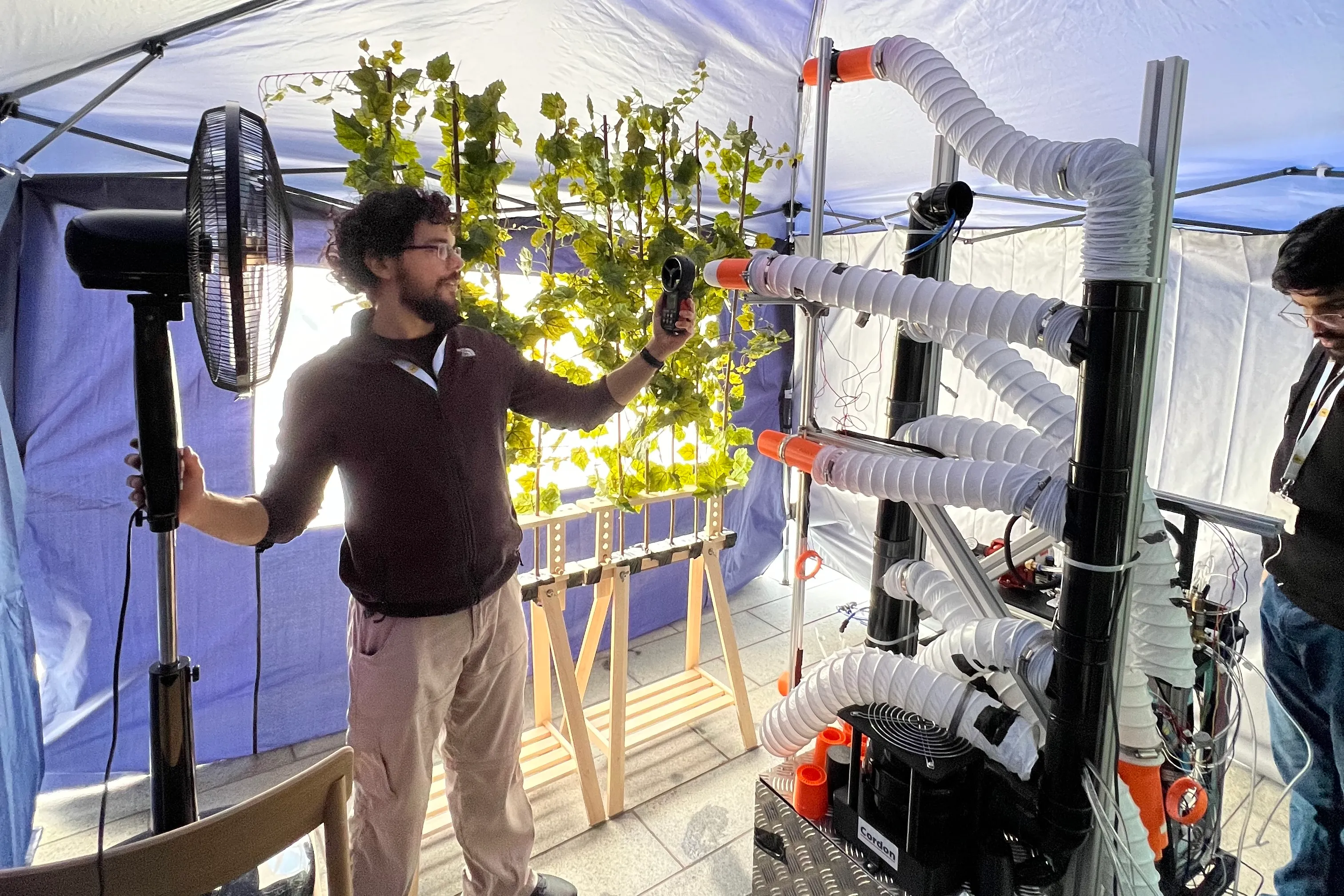 Members of the Cordon team testing a sprayer prototype with an artificial grapevine in a tent.