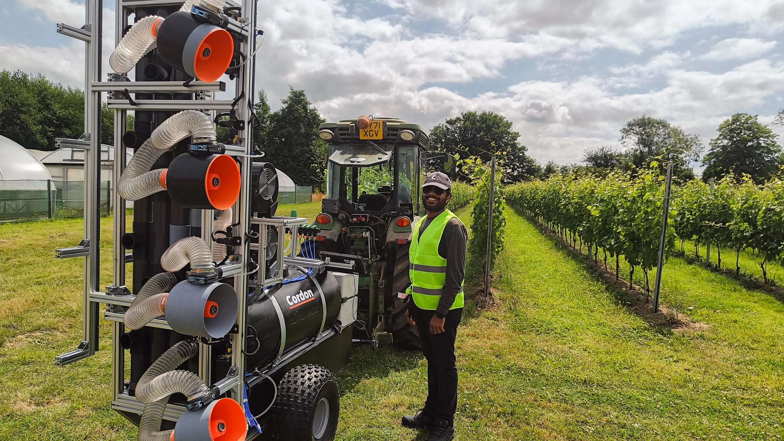 A man standing beside Cordon's vinyard sprayer robot in a green vineyard.
