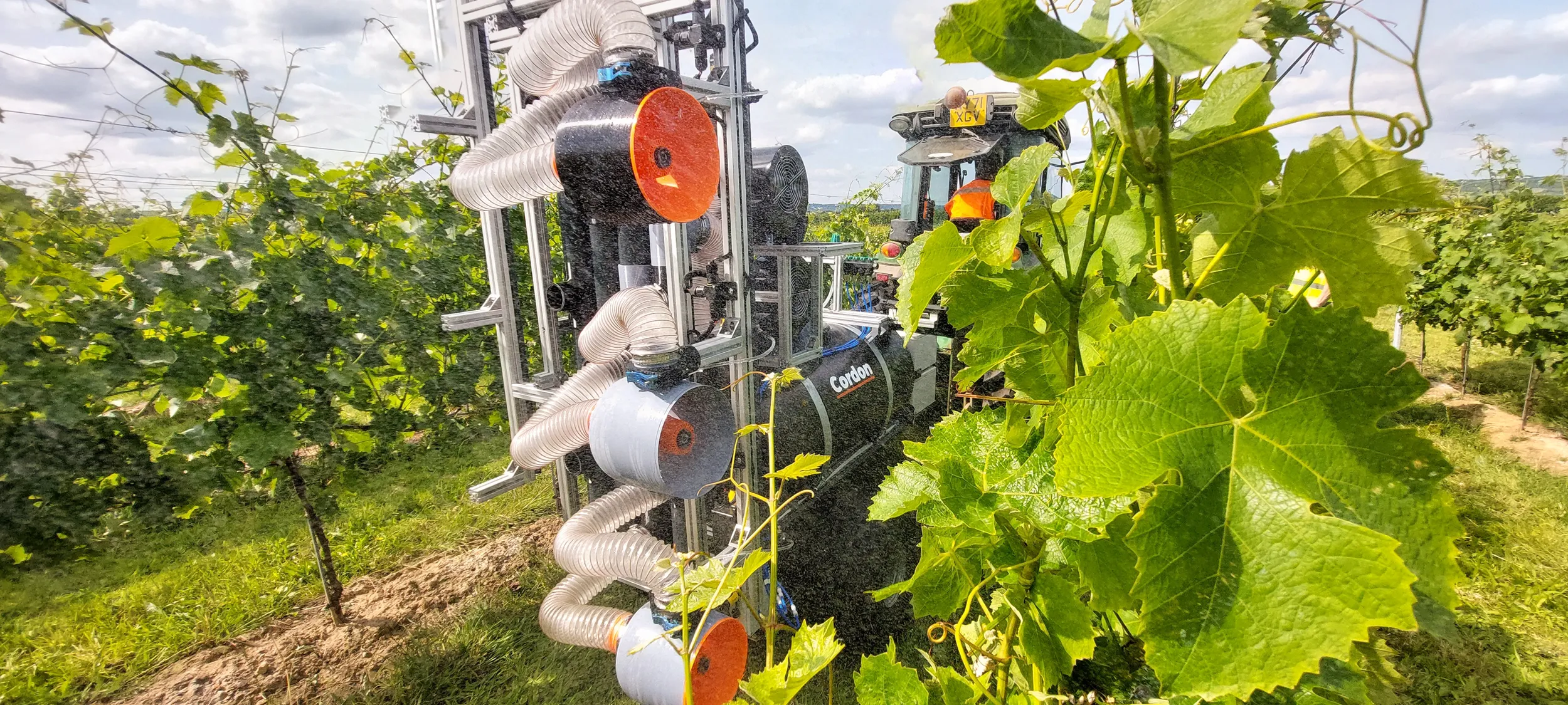 Cordon's vinyard sprayer robot being towed by a tractor in a green vineyard.