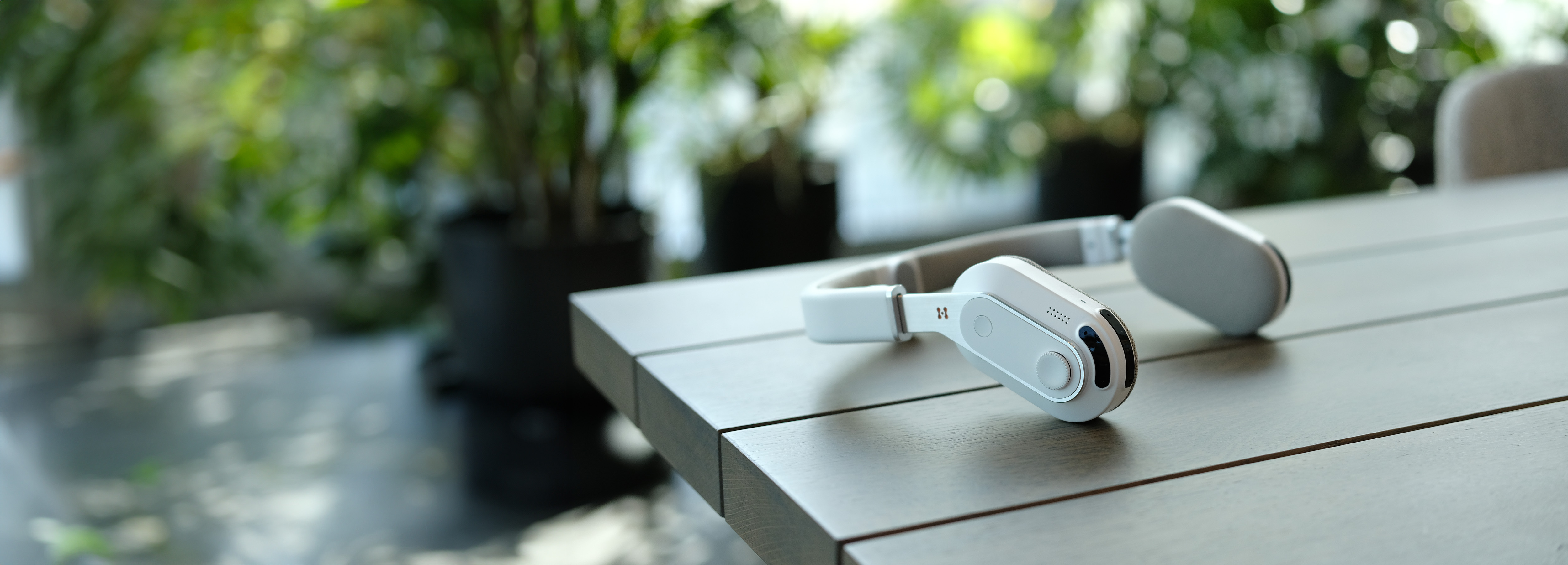 The Sixth Sense assistive wearable product for visually impaired people, placed on a brown wooden table with blurred foliage in the background.