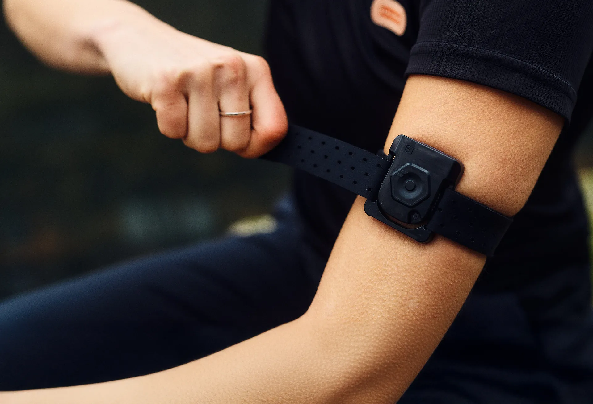 Person tightening a FLOWBIO smart hydration sensor onto their upper arm.