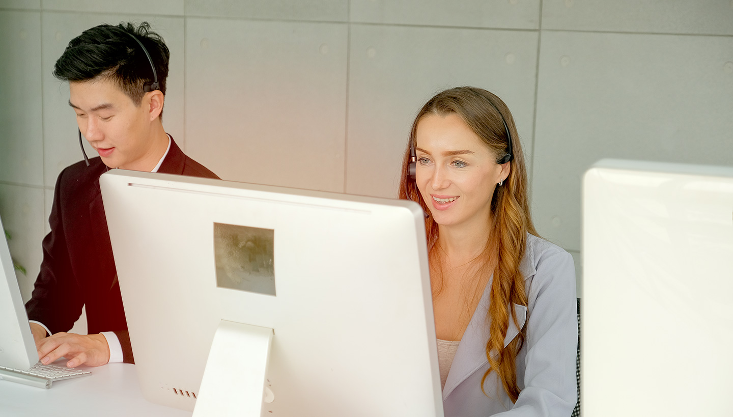 Two workers with headsets using desktop computers for cybersecurity audit services