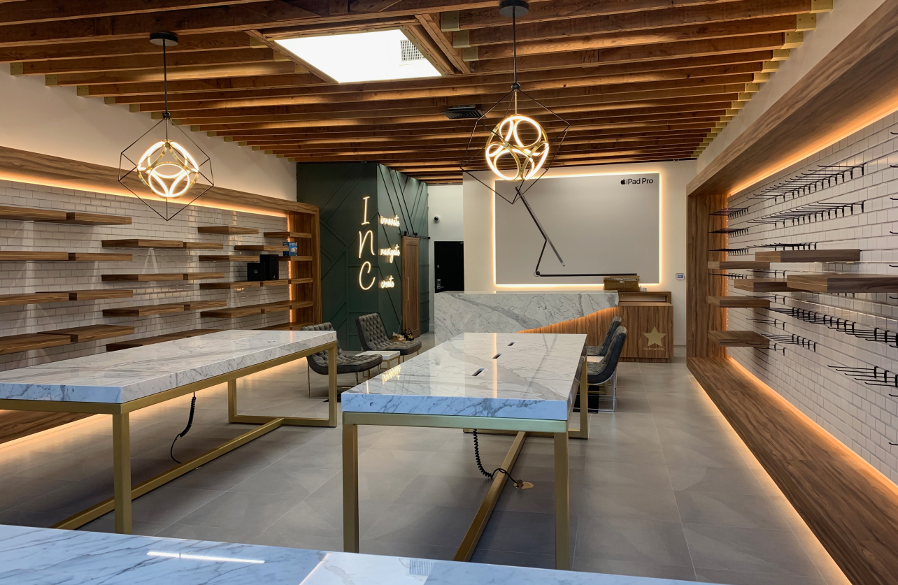 Modern retail interior with marble tables, wooden shelves, geometric pendant lights, and a neon sign reading 'innovate navigate create'.