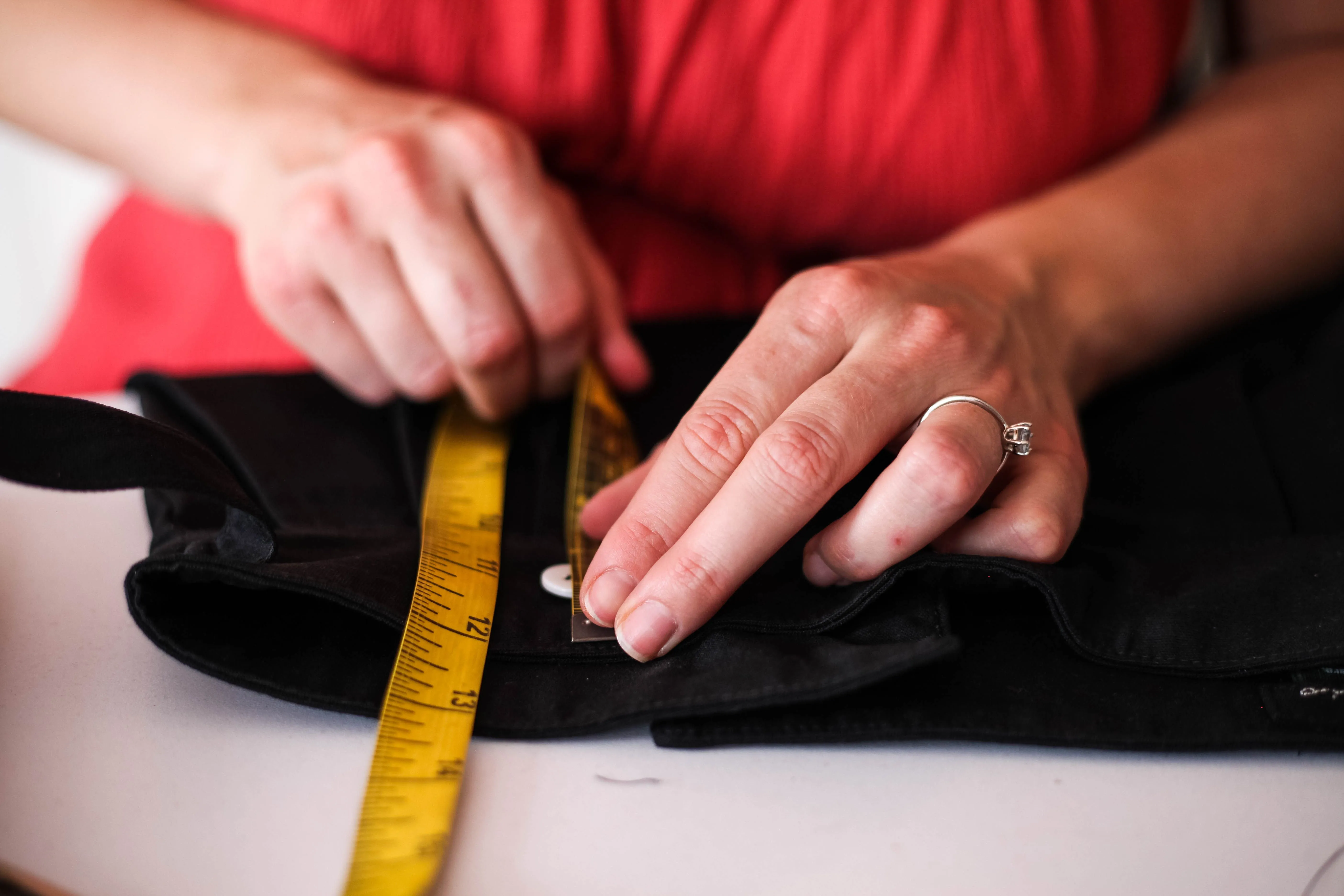 Hands measuring black fabric with a yellow tape measure near a white button.