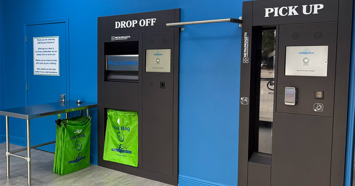 Black dry cleaning kiosk with drop off and pick up sections against a blue wall with green bags and stainless steel table.