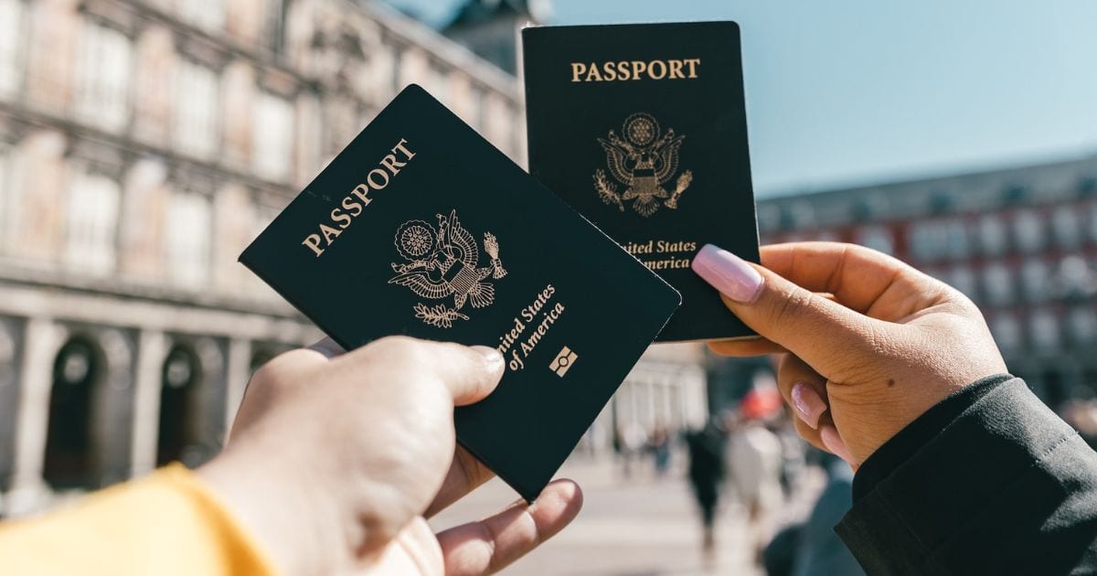 duas mãos segurando passaporte em frente a um monumento antigo