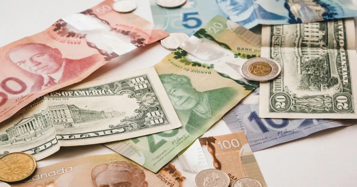 Diversas notas e moedas de dólar americano espalhadas sobre uma superfície branca