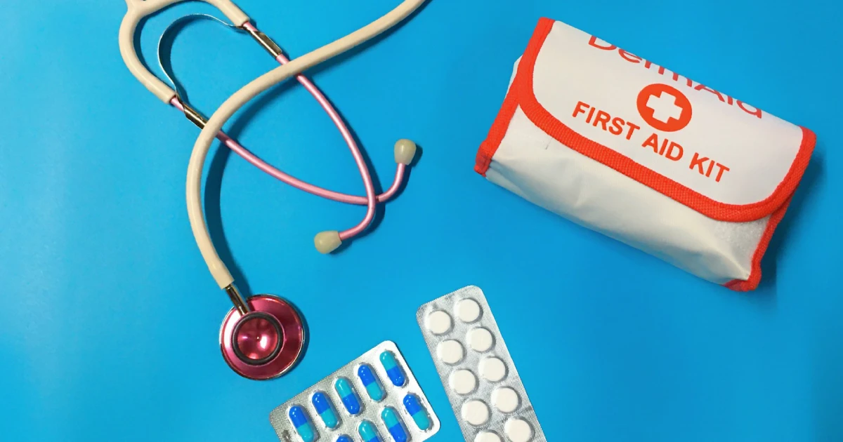 Estetoscópio, cartelas de medicamento e bolsa de primeiros socorros sobre uma superfície azul