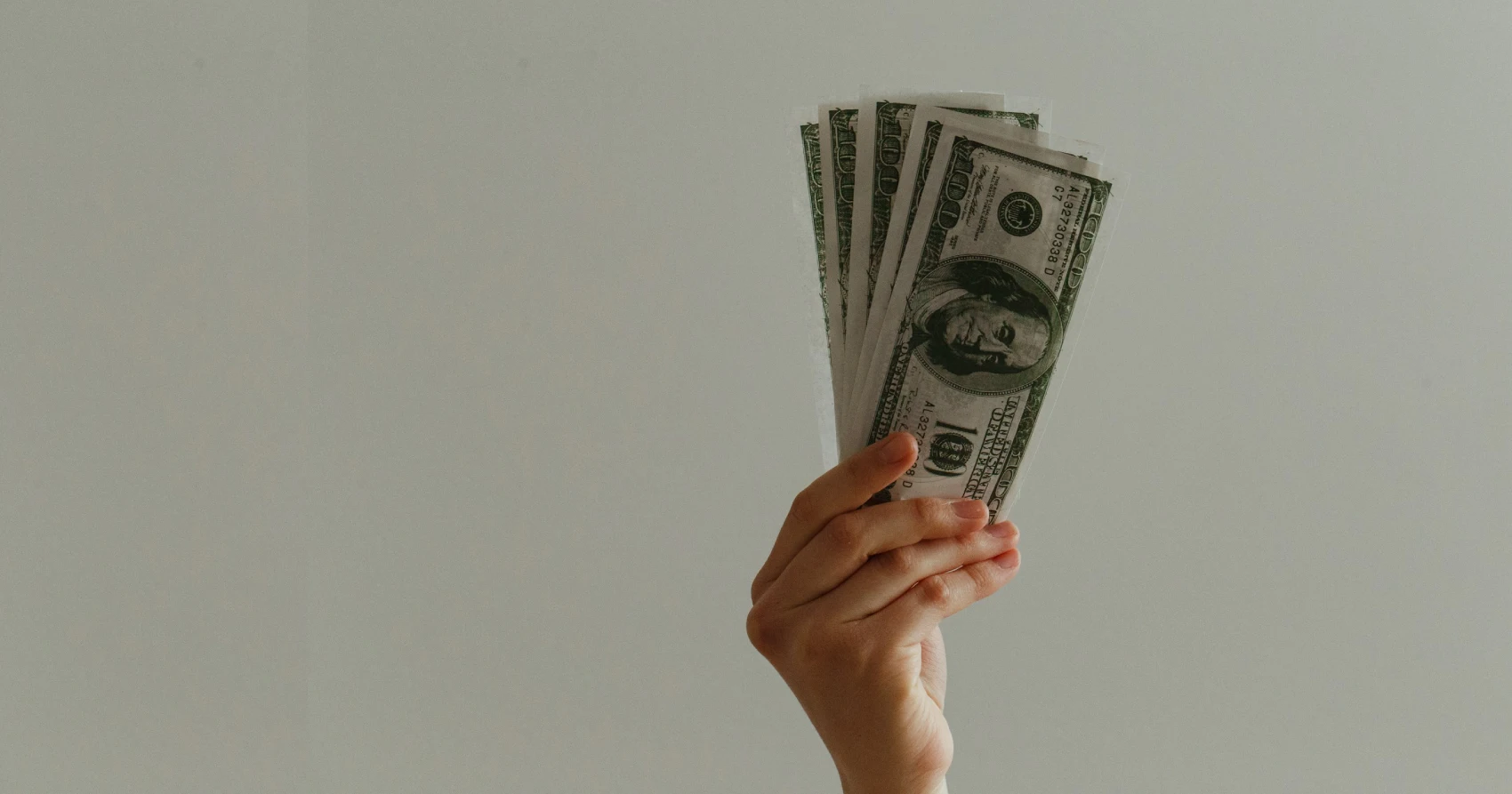 Pessoa segurando um maço com notas de dólar americano na mão